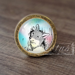 May include: A round, gold-colored cabinet knob with a glass insert featuring a black and white illustration of a dog's head against a colorful background.
