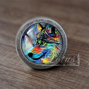 May include: A round, silver-toned cabinet knob with a colorful wolf design. The wolf is painted in shades of blue, green, yellow, and red.