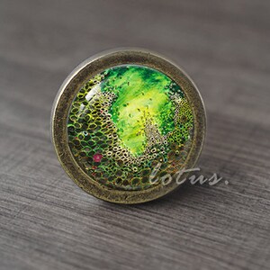 May include: A round, bronze-colored knob with a green and yellow abstract design inside a clear glass dome.
