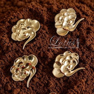 May include: Four gold-colored cloud-shaped decorative hardware pieces. Each piece has a layered, floral-like design with a curved, elongated element. The pieces are arranged on a textured, brown surface. The word "Lotus" is visible.