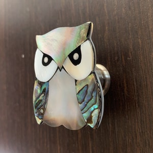 May include: A white and iridescent owl-shaped cabinet knob with a silver base.