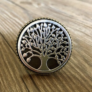 May include: A silver and brass round knob with a tree of life design. The tree is cut out of the metal and has a dark brown background.