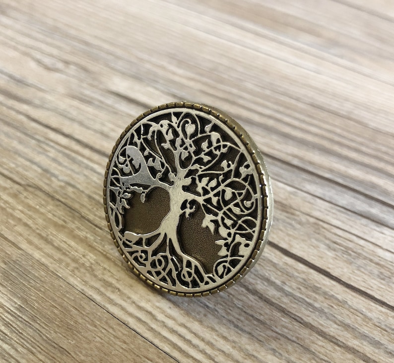 May include: A silver and bronze circular pendant with a tree of life design. The tree is intricately detailed with branches and leaves.