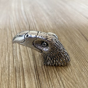 Pode incluir: Uma maçaneta de porta de prata em forma de cabeça de águia com penas detalhadas e um olho realista.