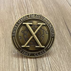 Peut inclure: Une pièce de monnaie en métal couleur or avec les mots "Xavier's School for Gifted Youngsters" et "First Class" autour du bord. Le centre de la pièce présente un grand "X" avec un motif circulaire.
