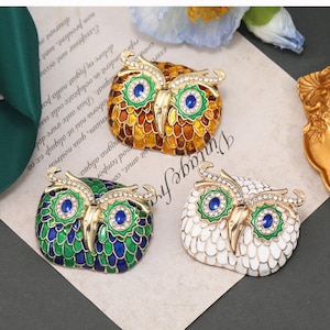 May include: Three owl-shaped brooches with jeweled eyes. The owls are made of metal and have a gold finish. One owl is green and blue, one is white, and one is orange and yellow.