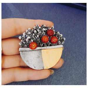 May include: A silver and gold brooch with a half-circle design. The brooch features a cluster of silver flowers with red gemstones in the center.