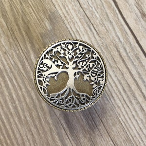 May include: A silver and gold tree of life design on a round knob. The knob is perfect for adding a touch of nature to your home decor.