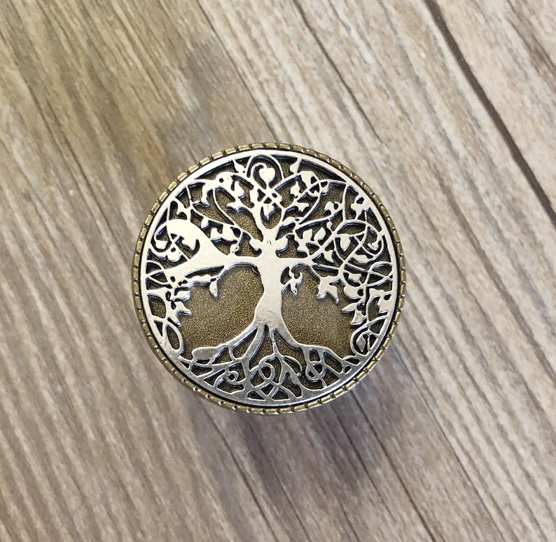 May include: A silver and gold tree of life design on a round knob. The knob is perfect for adding a touch of nature to your home decor.