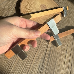 Könnte beinhalten: Schrankgriffe aus Holz mit rechteckigem Design. Die Griffe bestehen aus hellbraunem Holz mit einem silberfarbenen Metallakzent. Die Griffe werden auf einer Holzoberfläche gezeigt.