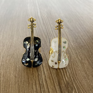 May include: Two decorative cello-shaped brooches, one black with white accents and one white with black accents.