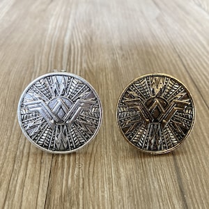 Puede incluir: Dos anillos de metal decorativos con un diseño geométrico. El anillo de la izquierda es plateado y el anillo de la derecha es dorado.