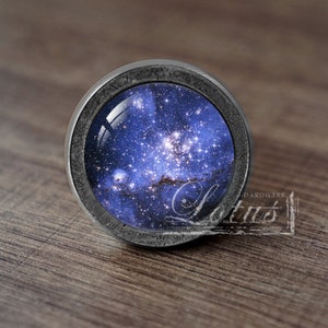 Może przedstawiać: Srebrny gałka z okrągłym wstawką szklaną przedstawiającą obraz niebieskiej i białej galaktyki.