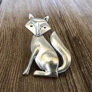 Könnte beinhalten: Eine silberne Fuchsfigur mit einem stilisierten Design. Der Fuchs sitzt mit seinem Schwanz um seinen Körper gewickelt.