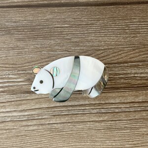 Puede incluir: Un broche de panda de madreperla blanca y gris con un dise&ntilde;o a rayas blanco y negro.