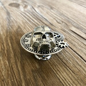 May include: Silver skull drawer pull with a clock face and gears. The skull is detailed with a stitched seam down the center of the head.