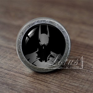 Könnte beinhalten: Ein silberner Knopf mit schwarzem Hintergrund und einer Silhouette von Batman in der Mitte.