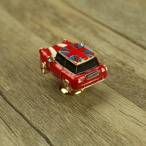 Może przedstawiać: Miniaturowy czerwony samochód z wzorem Union Jack na dachu. Samochód ma złote akcenty i jest ozdobnym gałką do szafki.