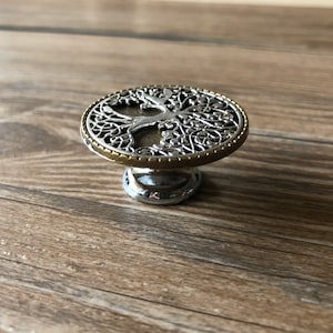 May include: A silver and gold metal cabinet knob with a tree of life design.