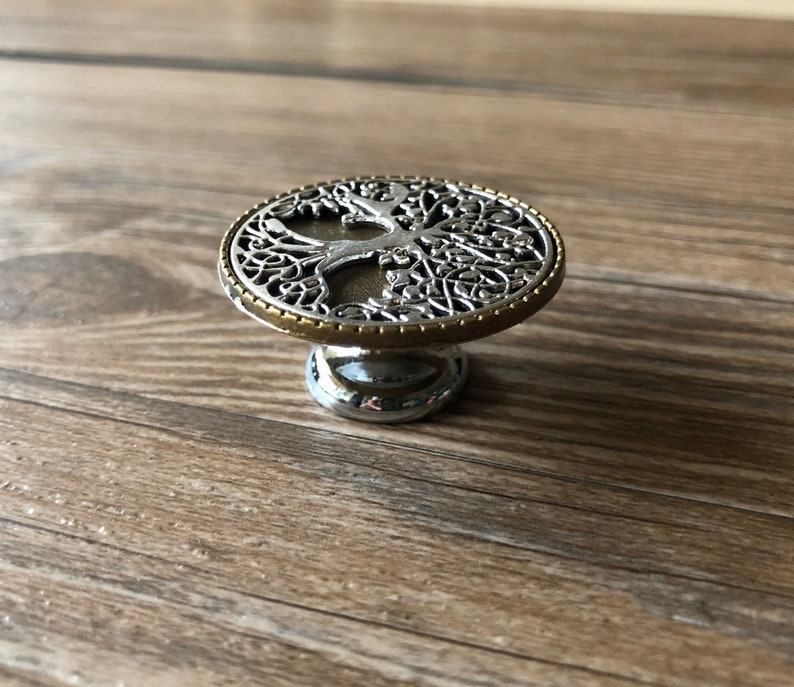 May include: A silver and gold metal cabinet knob with a tree of life design.