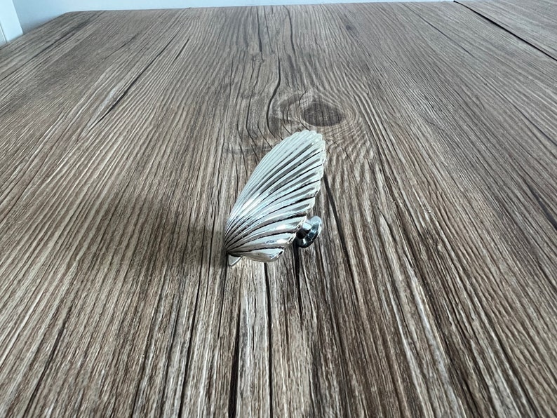 May include: Silver-toned seashell-shaped cabinet knob with a textured surface.