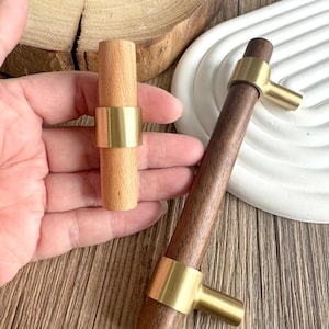 Peut inclure: Deux poignées de meubles en bois avec des détails en laiton. L'une est en bois clair avec une bande en laiton. L'autre est en bois foncé avec une poignée en laiton. Ces poignées décoratives sont pour les meubles et la décoration intérieure.