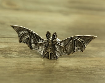 Può includere: Una maniglia o tirare per porta a forma di pipistrello di colore argento. Il pipistrello ha ali dettagliate e un corpo testurizzato.