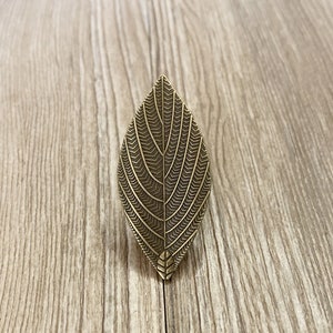 May include: A gold leaf-shaped decorative door knob with a detailed etched pattern.