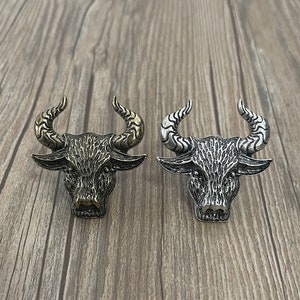 May include: Two metal bull head ornaments, one gold and one silver, with detailed textured designs.