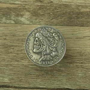 May include: A silver dollar coin featuring a skull and crossbones design. The coin is inscribed with the words "E. PLURIBUS UNUM" and "1878".