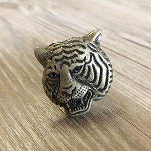 May include: A gold-toned metal tiger head drawer pull. The tiger's face is detailed with stripes and a snarling expression.