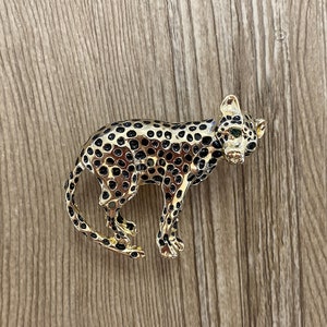 Peut inclure: Une broche dor&eacute;e en forme de l&eacute;opard avec des taches noires. Le l&eacute;opard a les yeux verts et un design d&eacute;taill&eacute;.