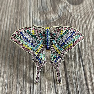 May include: A colourful butterfly brooch with a gold-tone finish. The butterfly is covered in iridescent rhinestones in shades of pink, blue, green, and yellow.