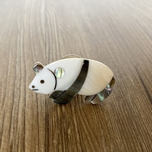 Puede incluir: Un broche de panda blanco y negro hecho de nácar con acentos iridiscentes.