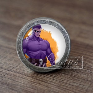 Könnte beinhalten: Ein runder, silberfarbener Schrank-Knopf mit einer lila und orangefarbenen Grafik eines Superhelden mit Maske. Die Grafik ist von einem weißen Rand umgeben.