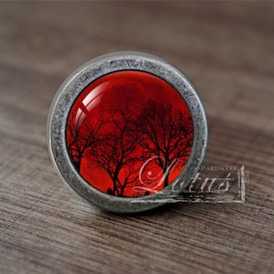 May include: A silver knob with a red and black image of trees silhouetted against a red sky.