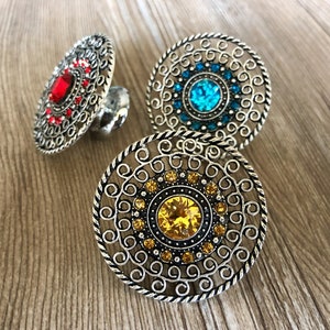 May include: Three silver rings with intricate designs and colorful gemstones. The rings feature a red, blue, and yellow gemstone in the center of each ring.