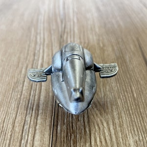 Peut inclure: Un vaisseau spatial jouet de couleur argent avec un corps arrondi et deux petites ailes. Le vaisseau spatial a un design détaillé et une finition métallique lisse.