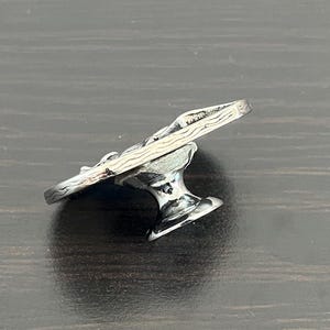 May include: A silver-colored, decorative cabinet knob with a detailed, textured design. The knob features a stylized, curved top and a pedestal base. The metal has a polished, reflective surface, and the design appears to be of a natural, organic form.