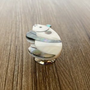 Puede incluir: Un pomo de armario de cer&aacute;mica blanco y gris con un dise&ntilde;o de oso panda. El panda est&aacute; hecho de n&aacute;car y tiene una piedra preciosa azul en la cabeza.