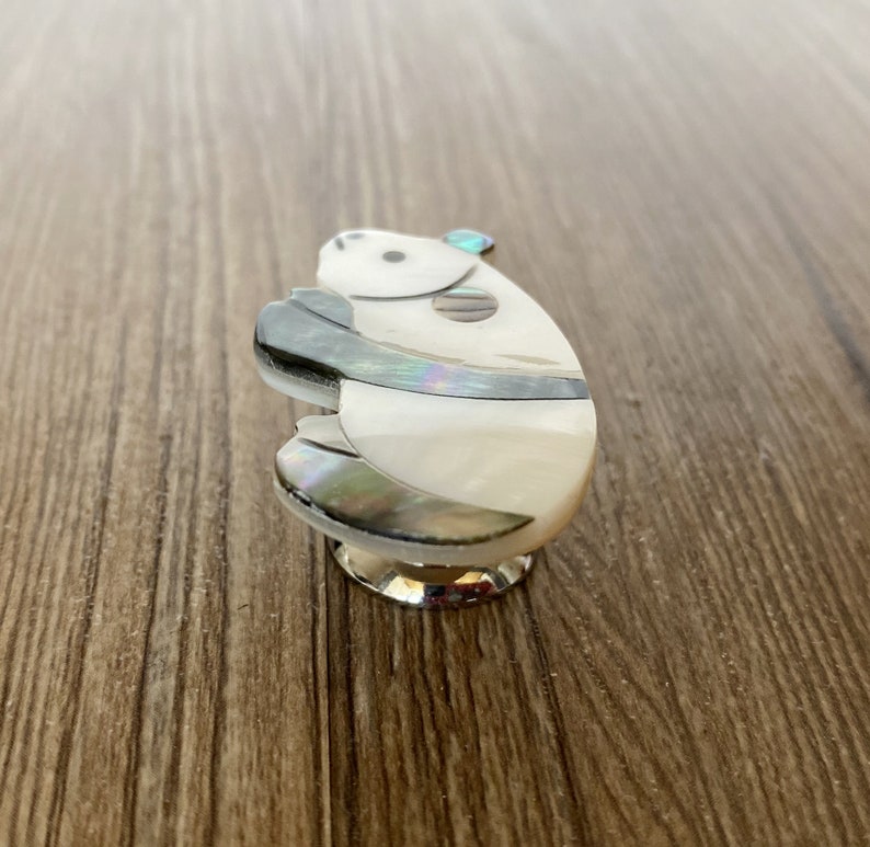 Puede incluir: Un pomo de armario de cer&aacute;mica blanco y gris con un dise&ntilde;o de oso panda. El panda est&aacute; hecho de n&aacute;car y tiene una piedra preciosa azul en la cabeza.