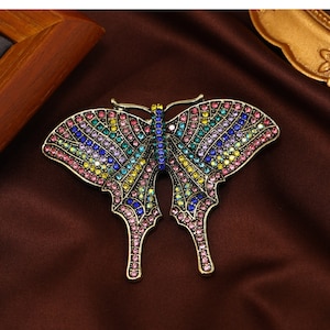 May include: A colorful butterfly brooch with a rainbow of rhinestones. The brooch is made of metal and has a vintage style.