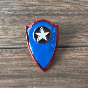 May include: A blue and red shield with a white star in the center. The shield is made of metal and has a glossy finish.