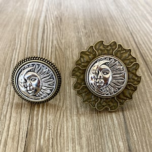 May include: Two decorative knobs featuring a sun and moon design. The knobs are made of metal and have a bronze finish. The sun and moon are silver and have a detailed design.