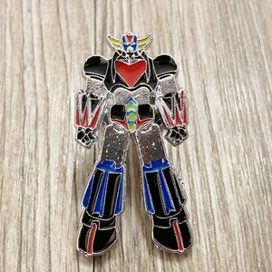 Könnte beinhalten: Eine silberne Roboter-Anstecknadel mit roten, blauen, gelben und grünen Akzenten. Der Roboter hat eine herzförmige Brust und eine Krone auf dem Kopf.