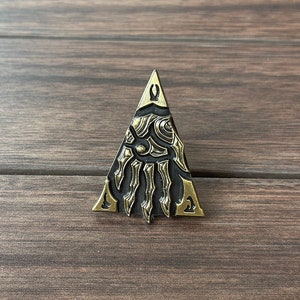 May include: A triangular metal pin with a gold finish. The pin features a detailed design of a skeletal hand with a black background.