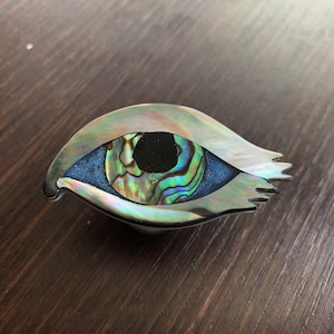 May include: A decorative eye-shaped trinket made of iridescent abalone shell with a blue and green center.