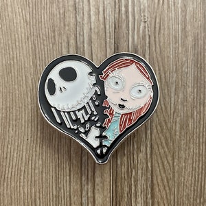 May include: A black and red heart-shaped pin with a white and black image of Jack Skellington and Sally from the Nightmare Before Christmas.