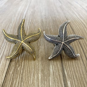 May include: Two decorative starfish drawer pulls, one gold and one silver. The starfish have a textured surface and are a popular choice for nautical themed decor.