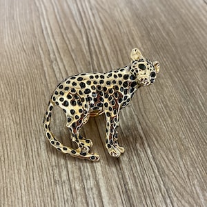 May include: A gold-colored leopard figurine with black spots and green eyes. The figurine is standing on a wooden surface.
